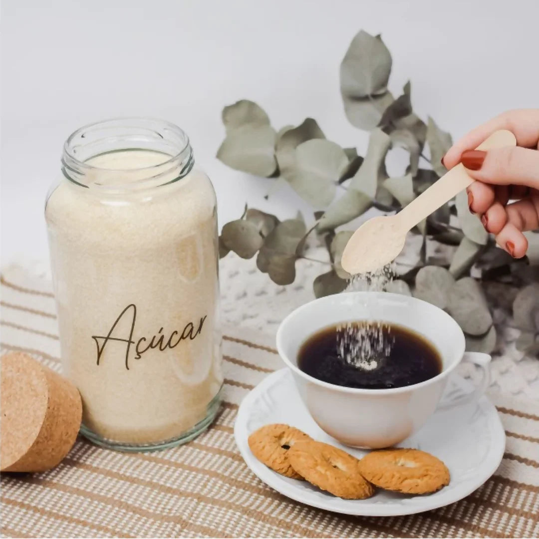Potes de vidro organizados em uma bandeja de madeira, decorando um espaço de café moderno com máquina de espresso ao fundo.